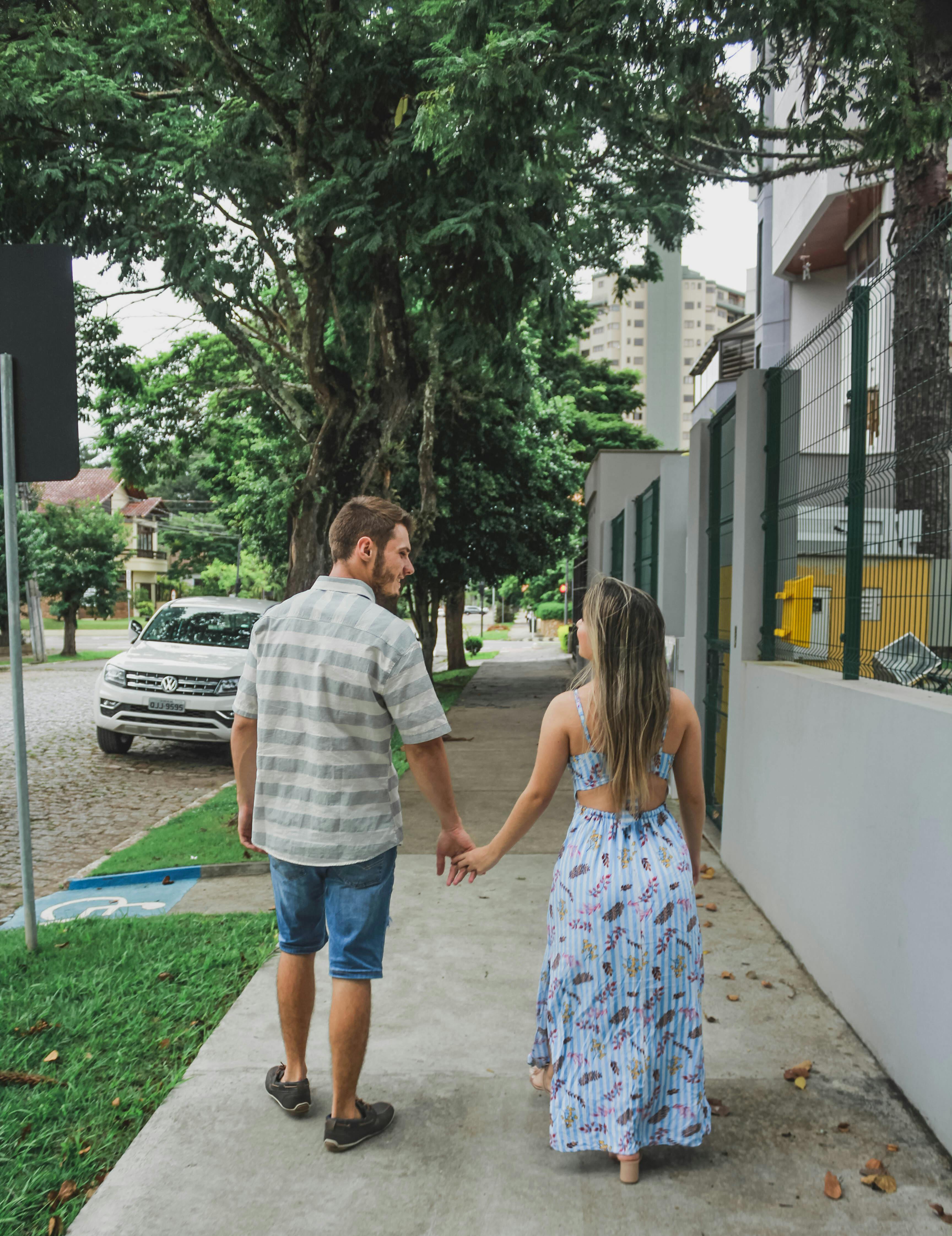 一对年轻男女手牵着手，走在城市街道旁的树荫下