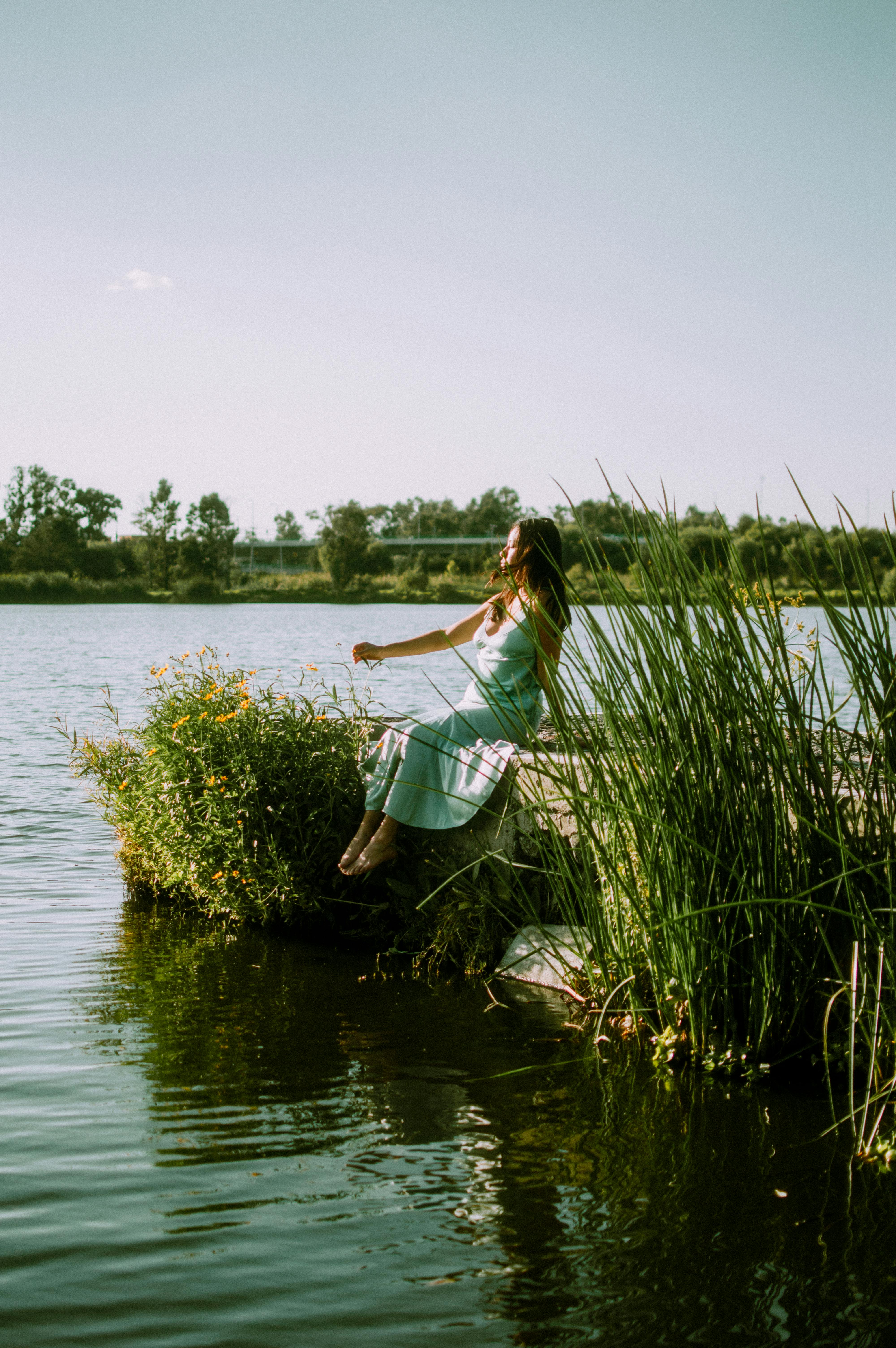 A young woman in a dress enjoying nature by a lake in Mexico during a sunny summer day.