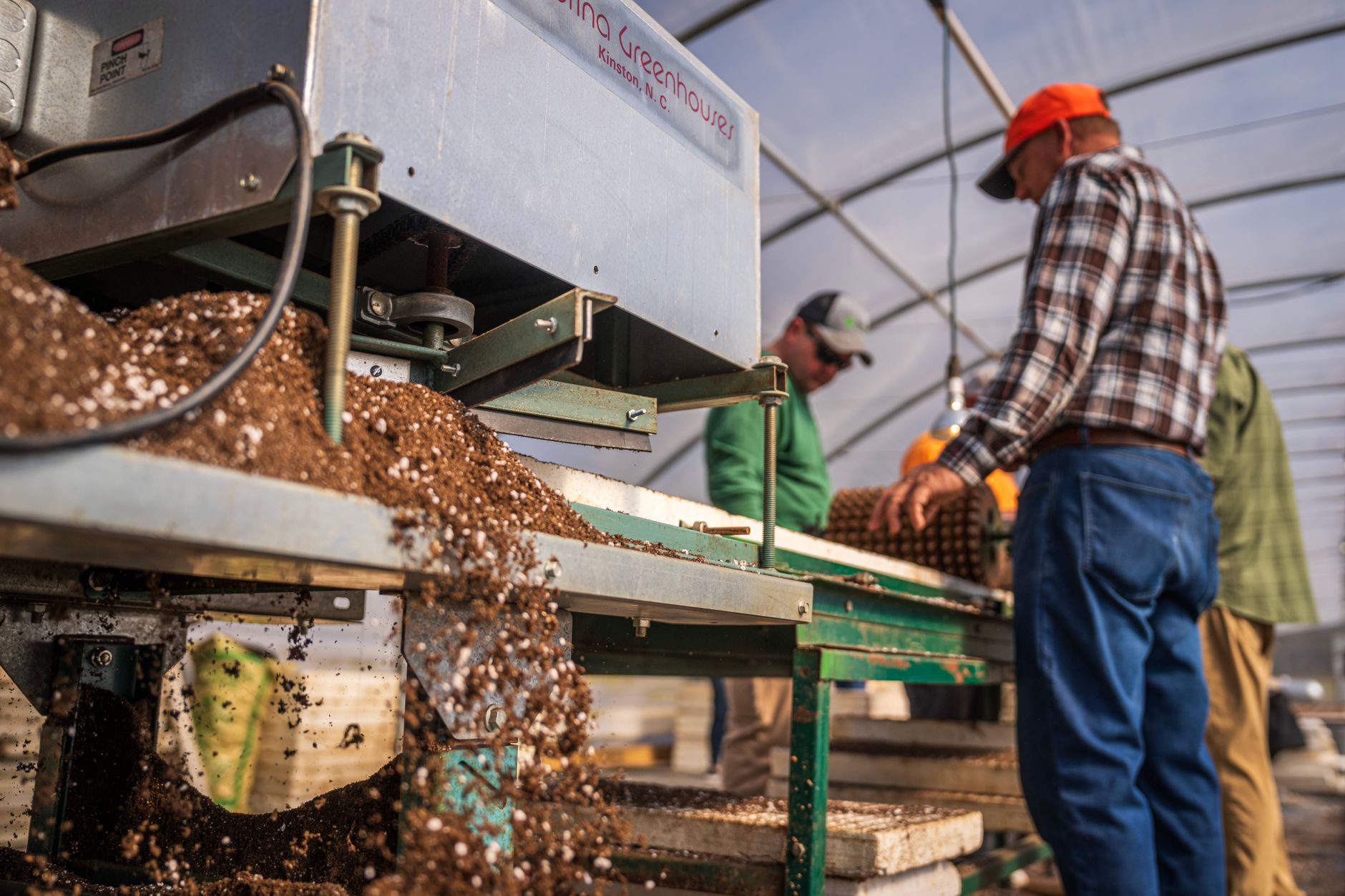 Workers operating machinery in a greenhouse for soil production.