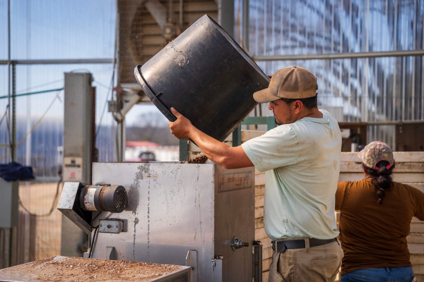 Worker pouring material from a bucket into industrial processing equipment