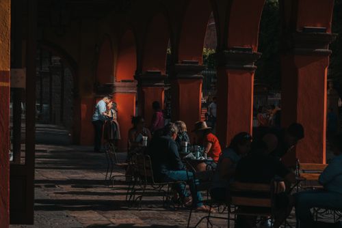 Free A couple shares a kiss beneath a vibrant archway in a bustling outdoor cafe scene. Stock Photo