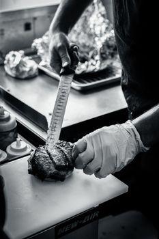 Close-up of a chef slicing meat in a professional kitchen setting, captured in black and white.