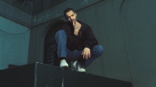 A man sitting on top of a ledge with his hands on his knees