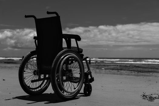 Black and white image of a wheelchair on a beach, symbolizing freedom and solitude.