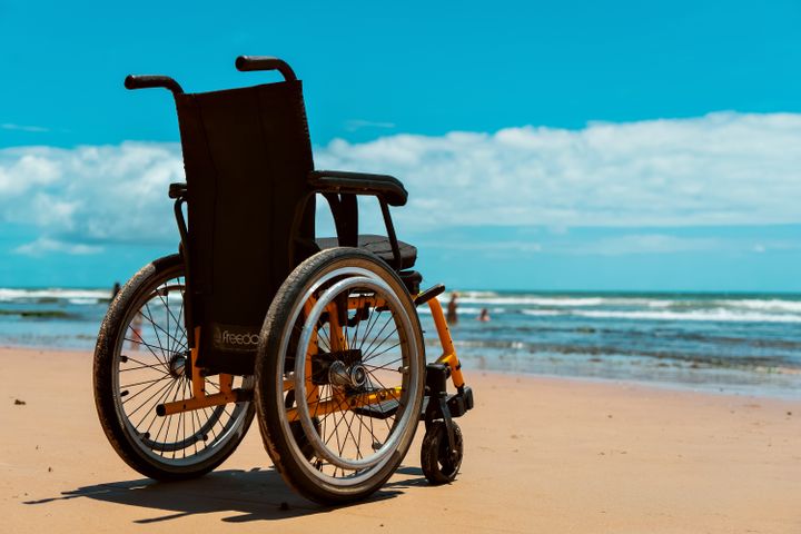 A wheelchair on a sandy beach overlooking the sea on a bright summer day.