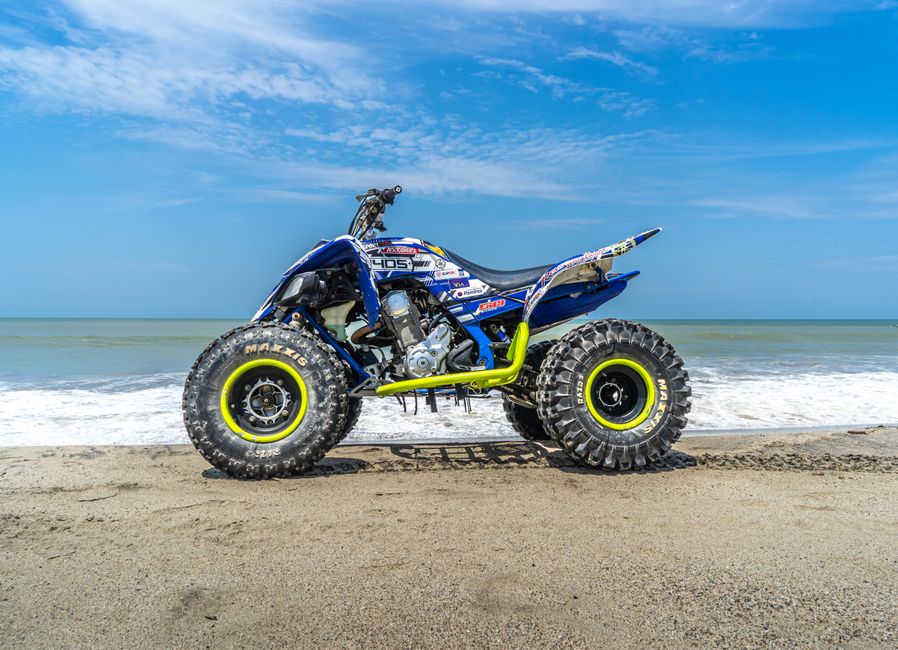 A detailed image of a quad bike parked on a sandy beach under a clear blue sky.