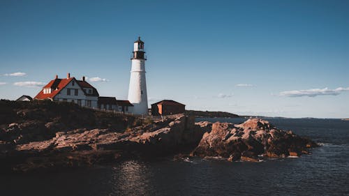 Foto de archivo gratuita de un faro en una costa rocosa con un cielo azul