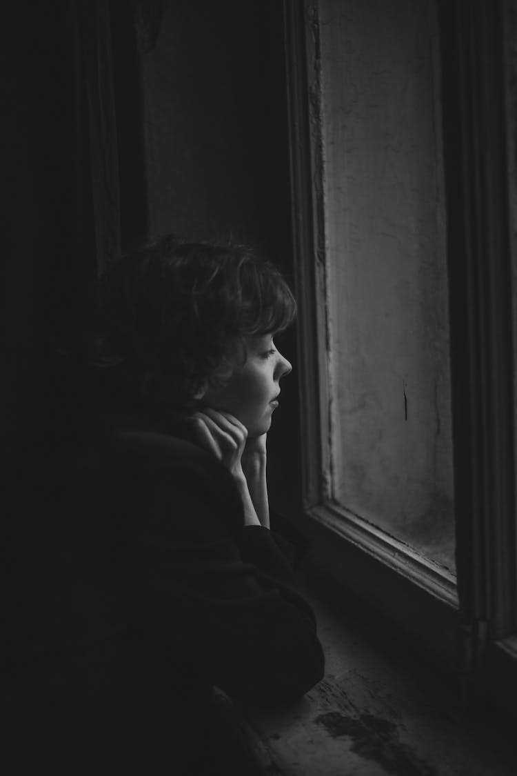 Young Woman Looking In Window In Dark Abandoned Building