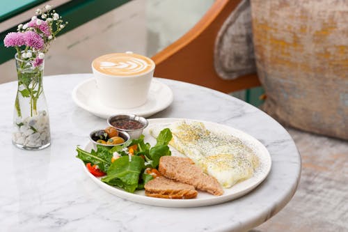 A white table with a plate of food and a cup of coffee