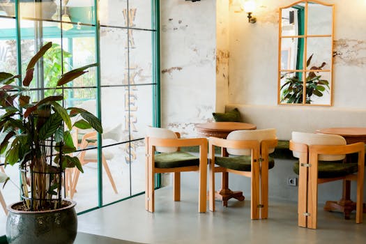 Modern cafe interior design featuring wooden chairs, large mirror, and lush green plants.