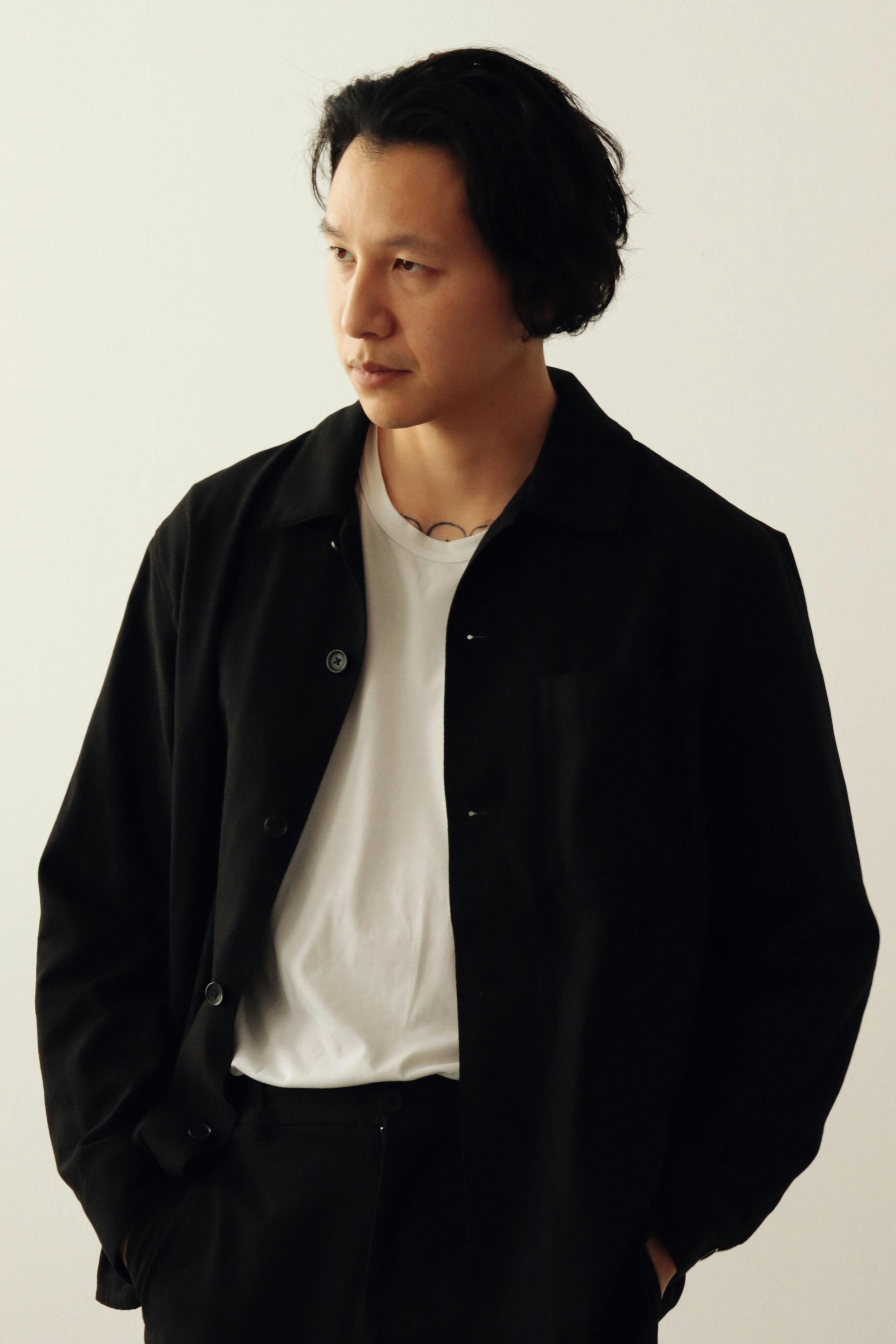 Portrait of an Asian man in a black jacket and white t-shirt, studio setting.