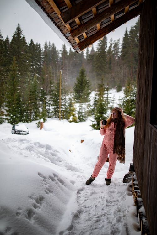 A woman in pink pajamas standing in front of a cabin