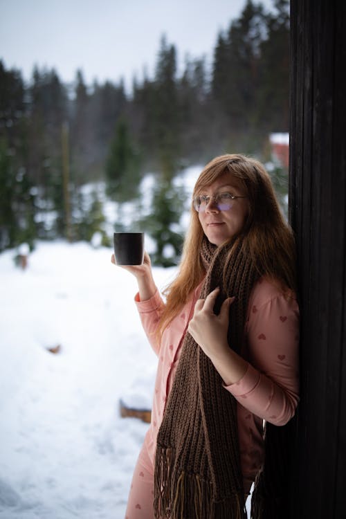 A woman in glasses holding a cup of coffee in the snow