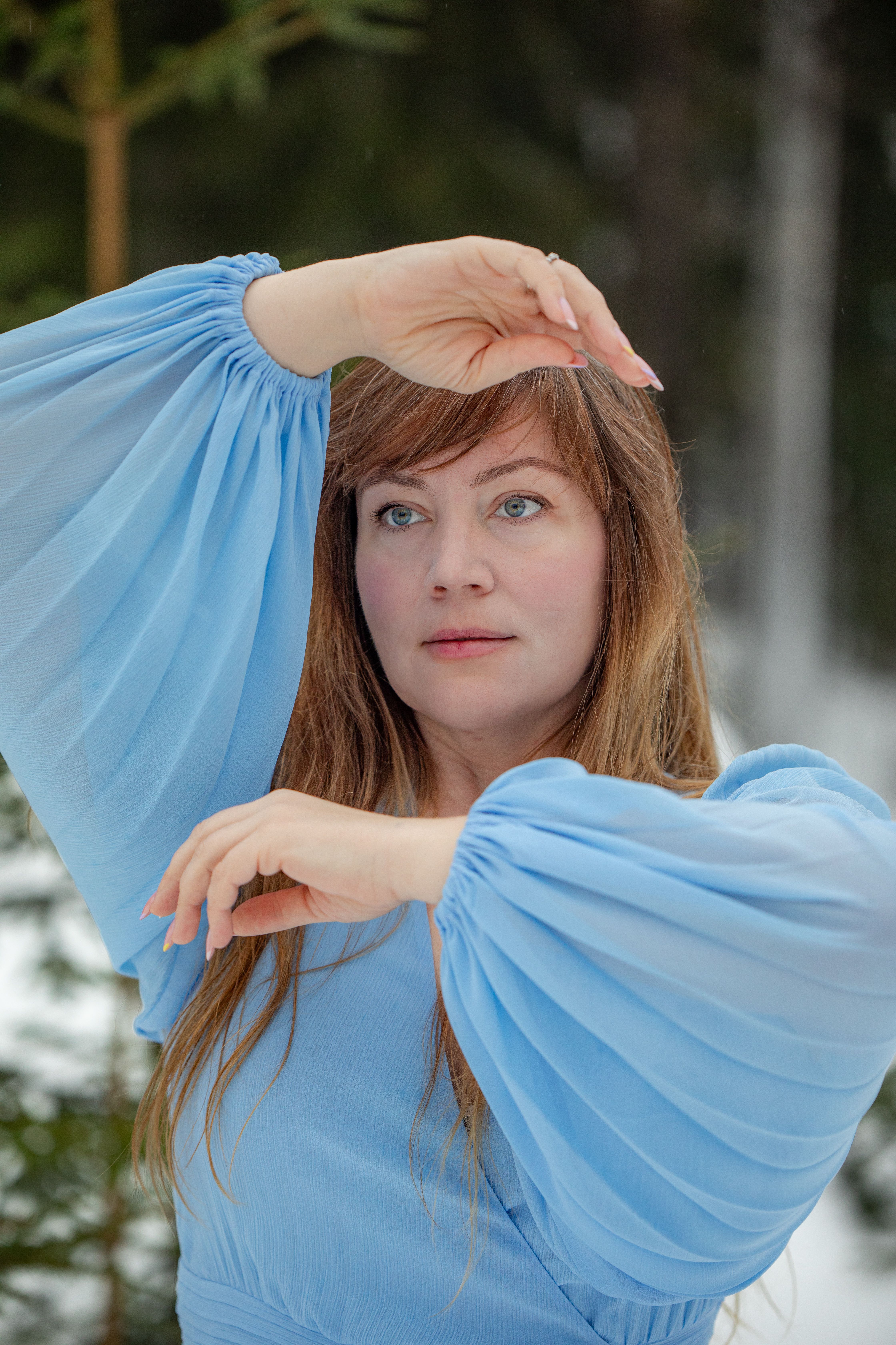 A woman in a blue dress posing elegantly outdoors during winter.