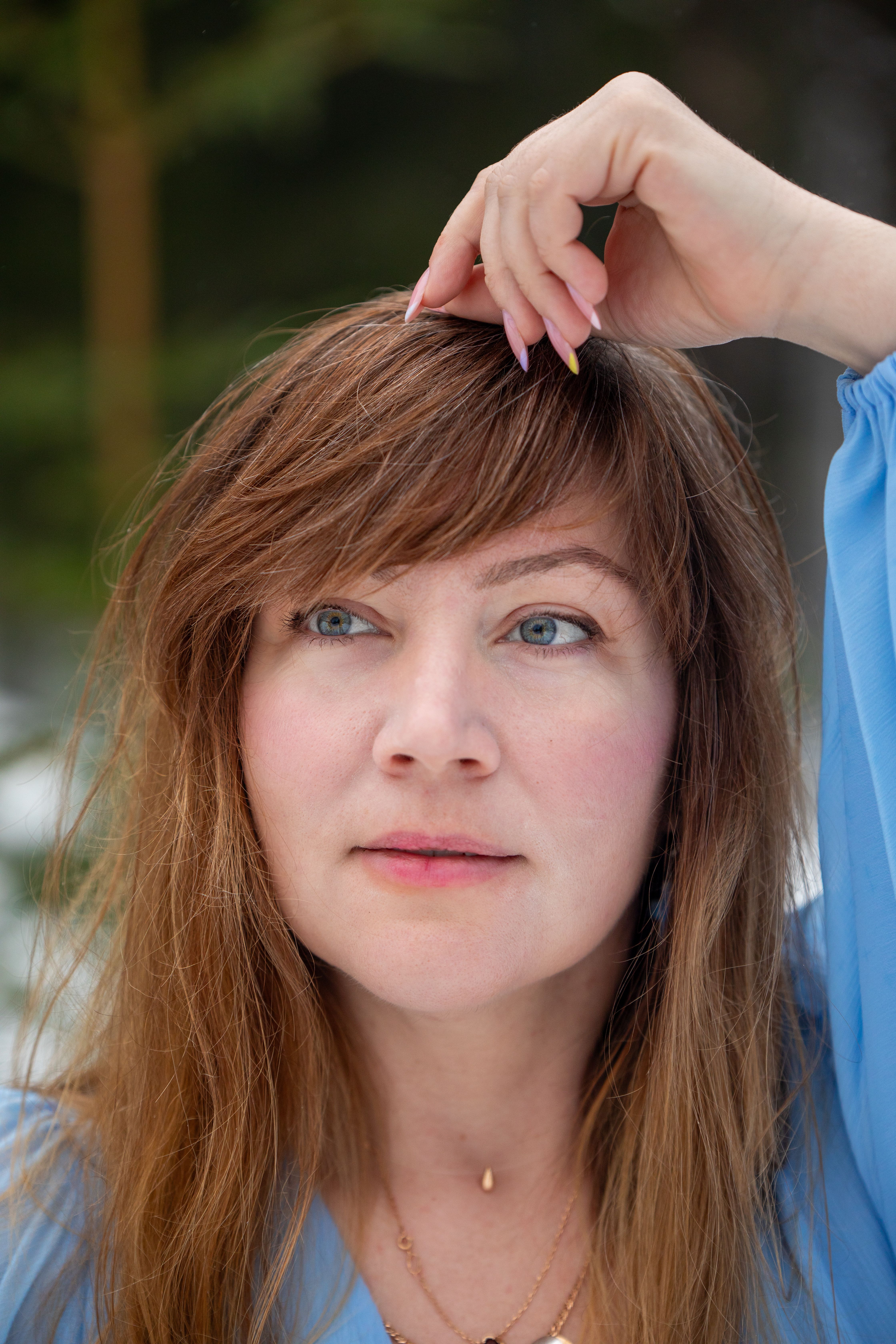 Close-up portrait of a woman fixing her hair outside, showcasing natural beauty.
