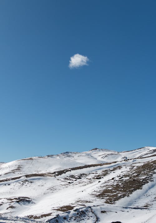 A lone cloud in the sky over a snowy mountain