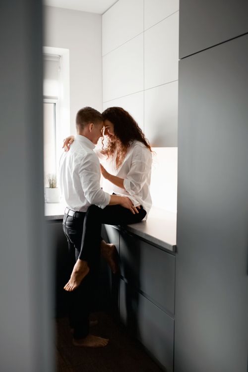 Free A loving couple shares an intimate moment in a bright, modern kitchen setting. Stock Photo