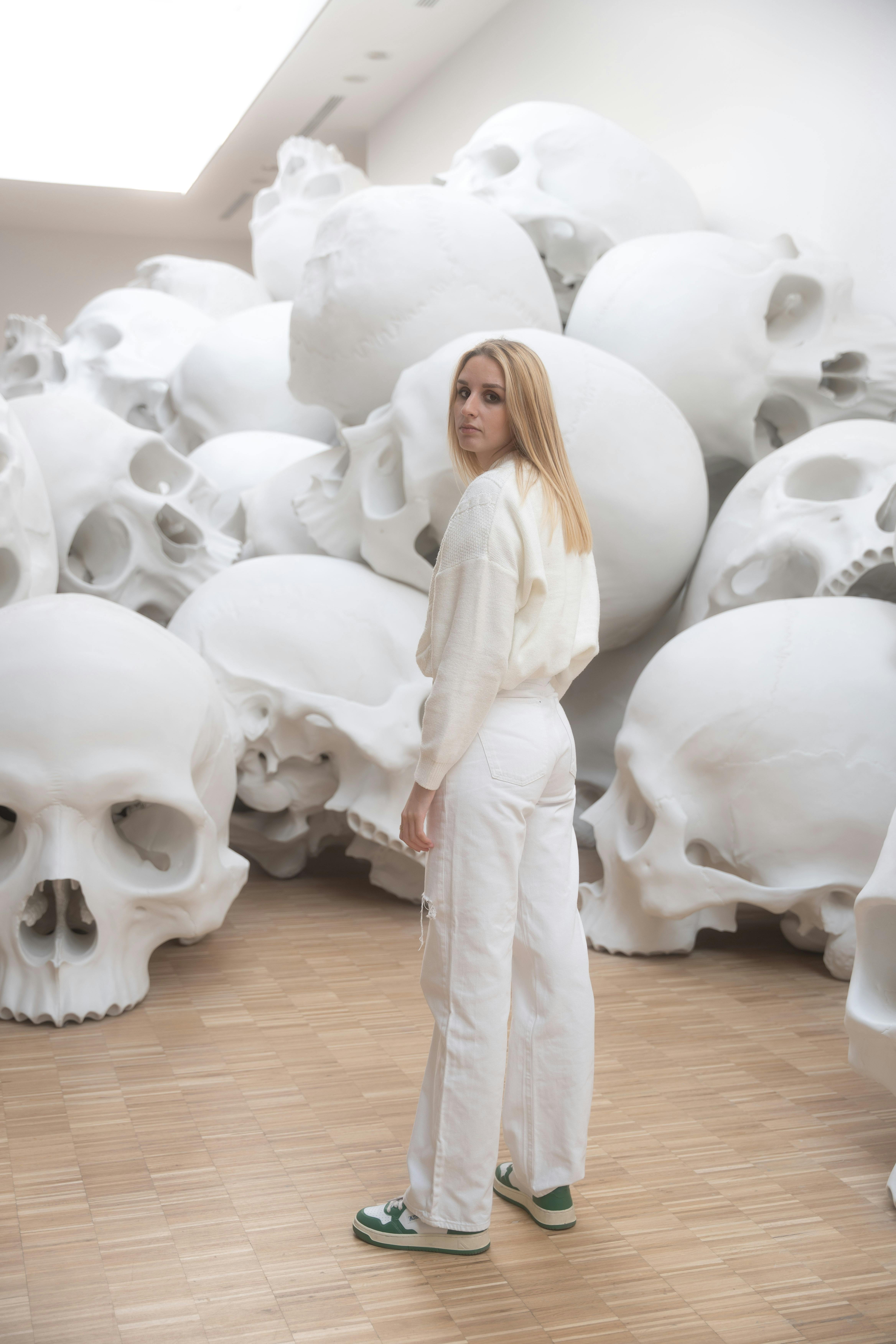 Woman standing among massive skull art installation, Milano gallery.