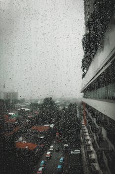 Raindrops on a window with an overcast urban view in Jakarta, Indonesia.