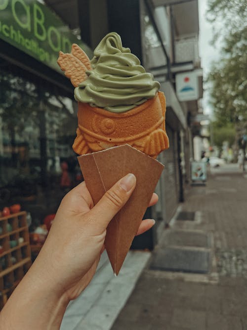 A person holding an ice cream cone with green and white toppings