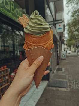 Hand holds matcha ice cream in fish-shaped cone on urban street.