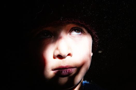 Close-up portrait of a child in dramatic lighting with shadows creating an artistic effect.