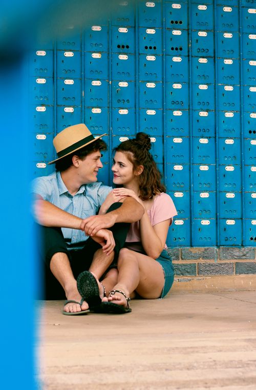 Free A young couple sits together, sharing an intimate moment against a vibrant blue wall. Stock Photo