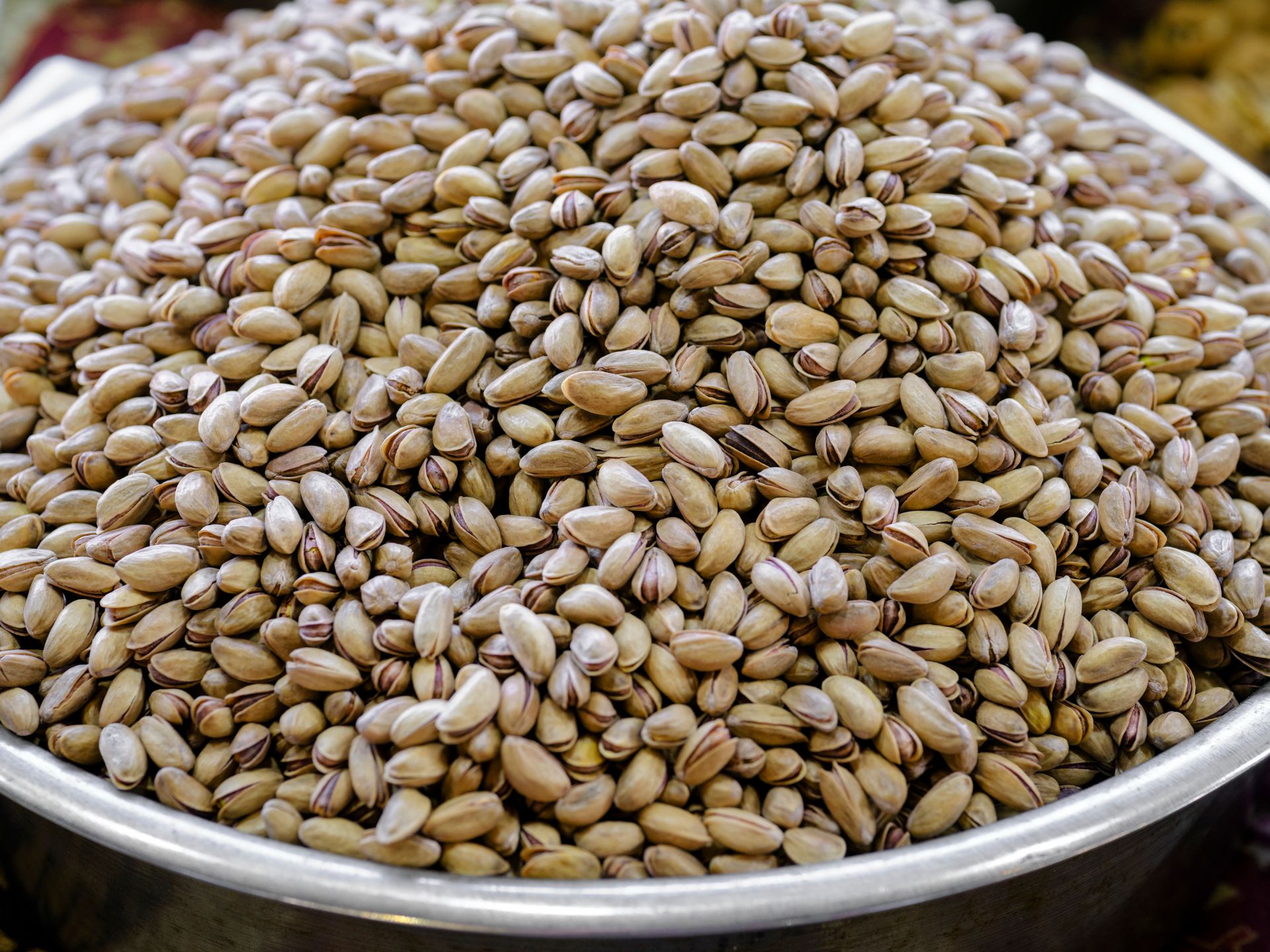 A close-up view of a large heap of pistachios in a stainless steel bowl, showcasing food abundance.