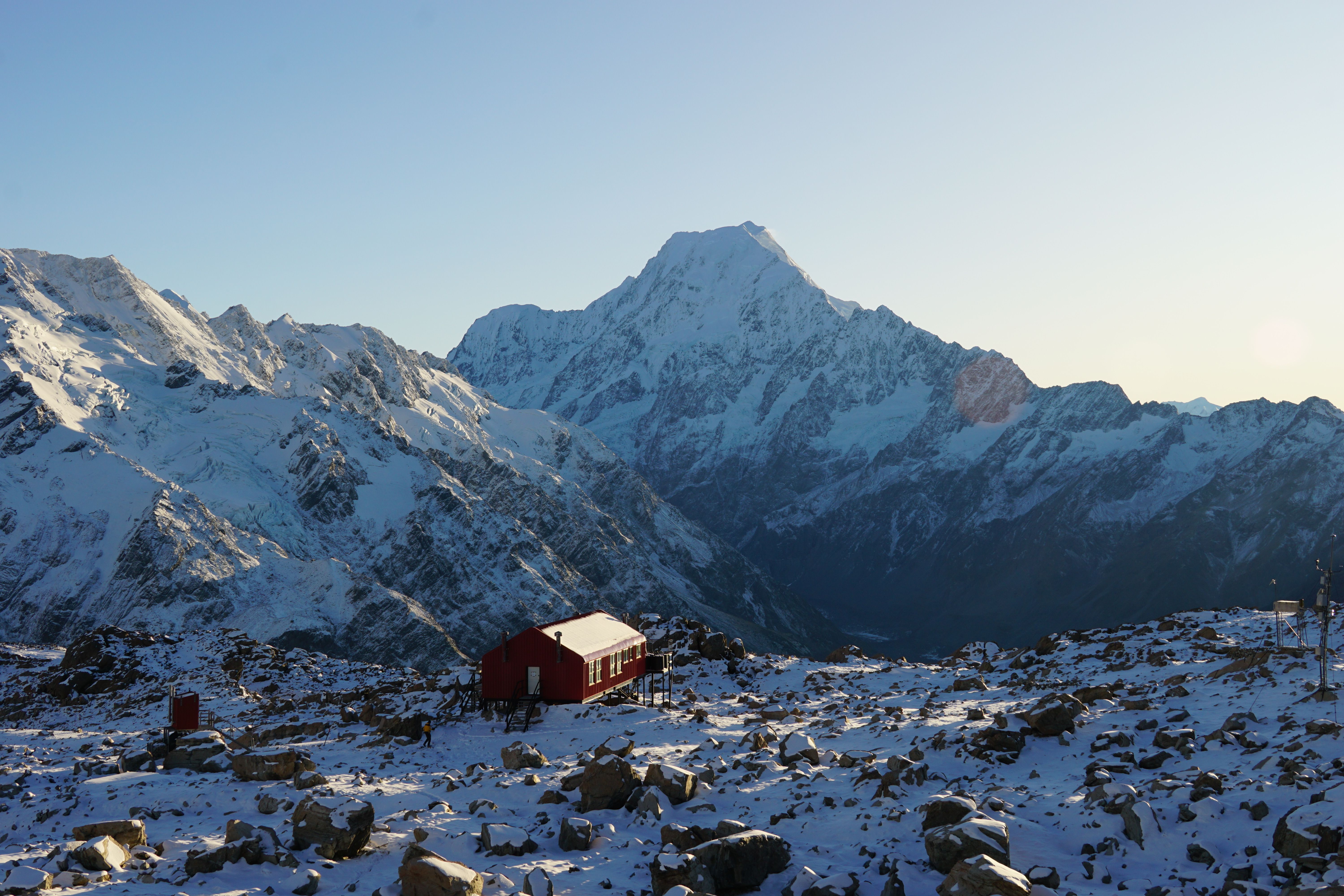 A red cabin nestled in a snow-covered mountain range during sunrise, offering a serene landscape view.