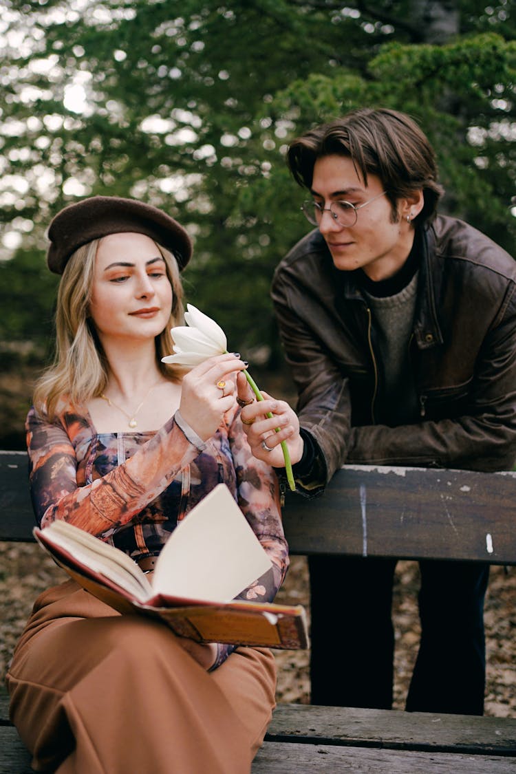 Young Man Giving Flower To Woman Reading In Park