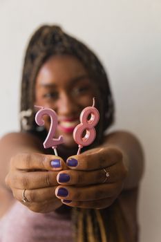 Close-up of a smiling woman holding colorful 28th birthday candles on a white background.