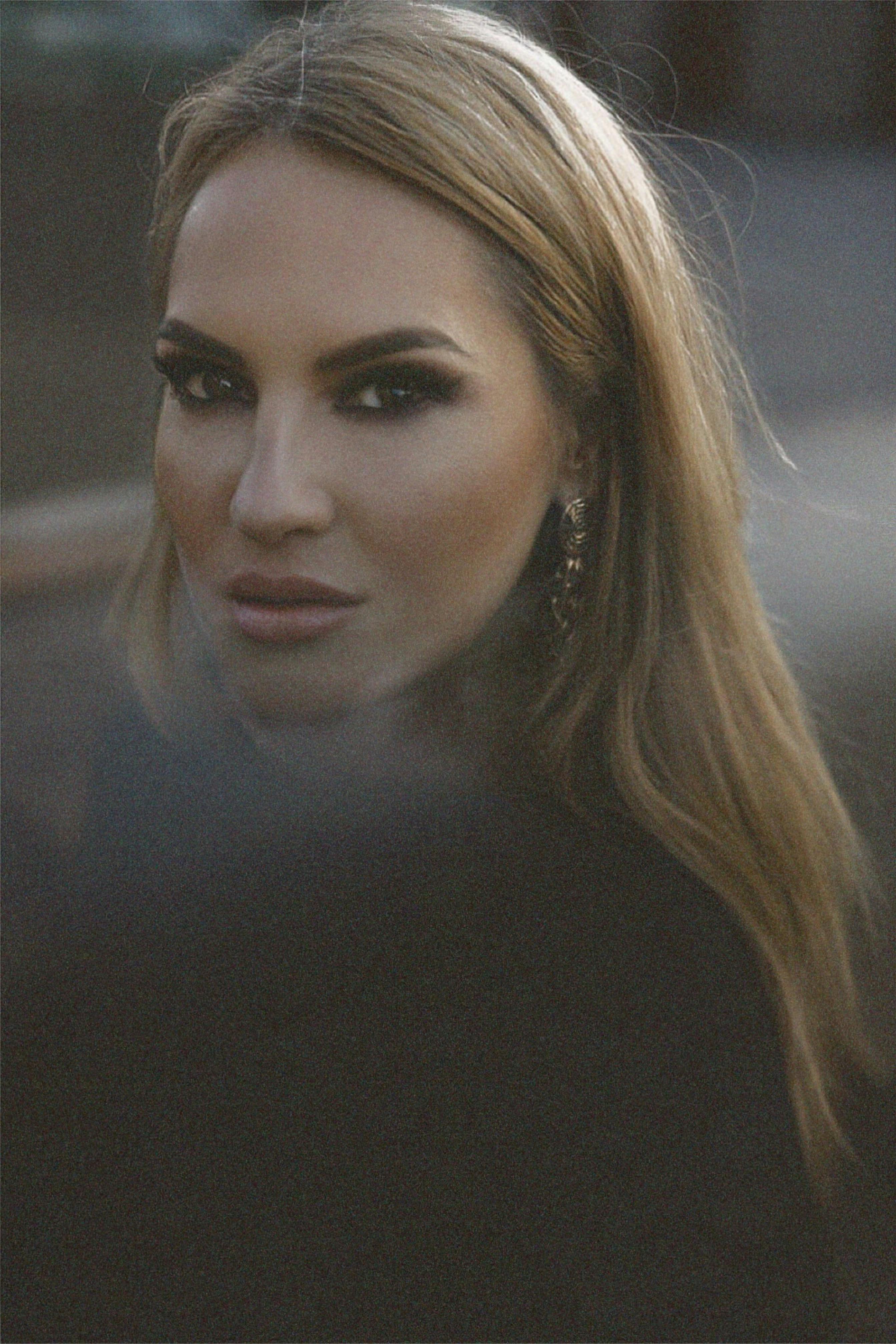 Portrait of a woman with makeup and long hair in soft natural light, emphasizing elegance.