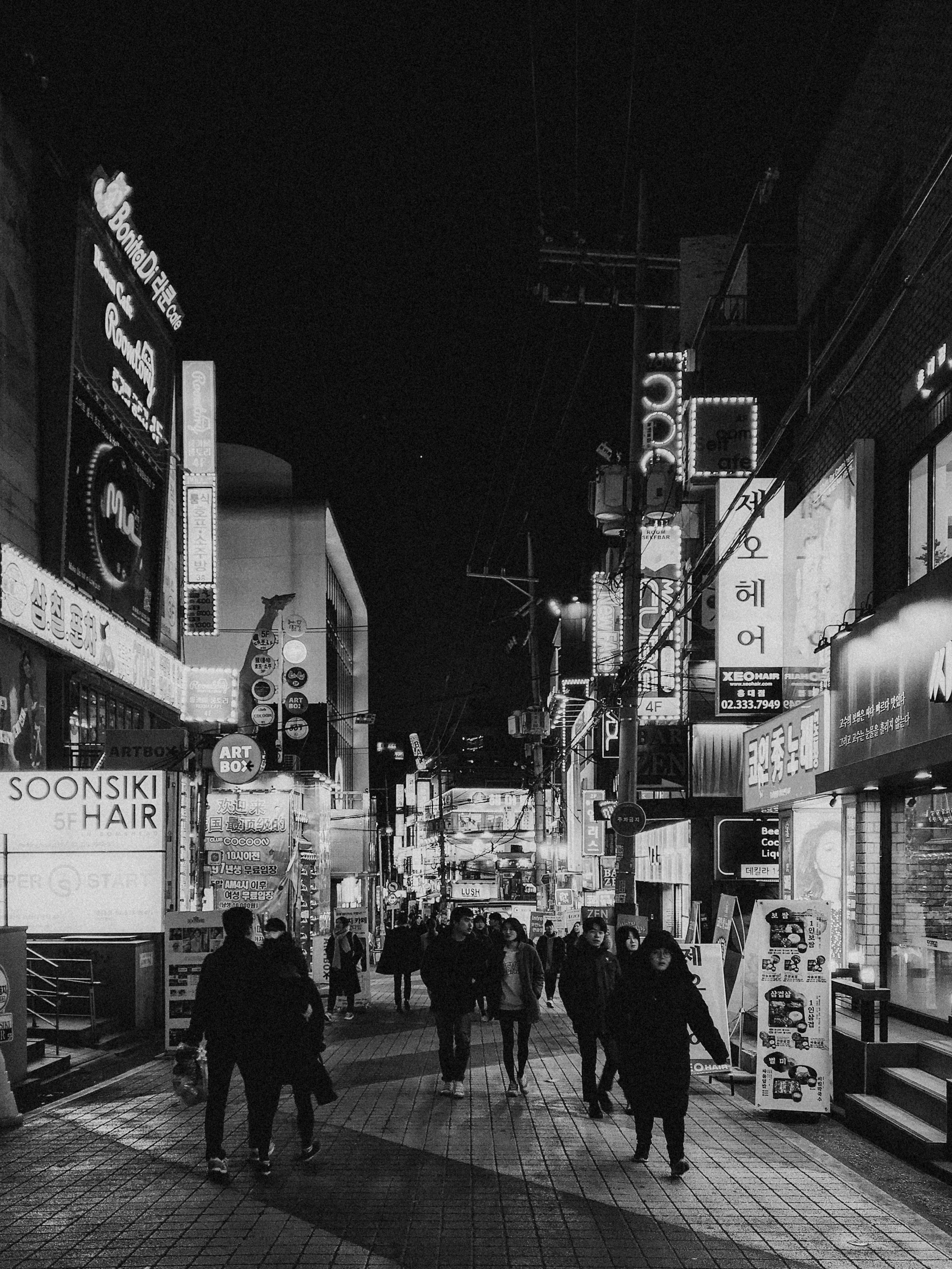 Black and white street scene capturing a bustling urban night life with neon signs and people in the city.