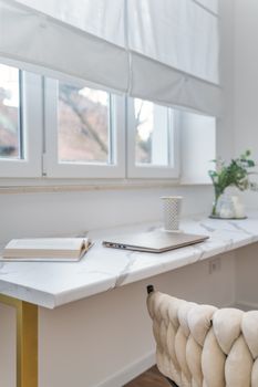 Elegant minimalist workspace with laptop and book by a bright window.