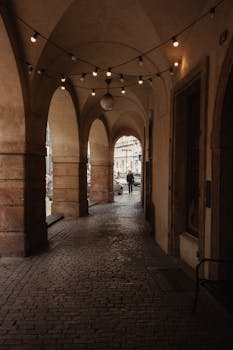 Rustic arched corridor in Prague with string lights and cobblestone pavement.