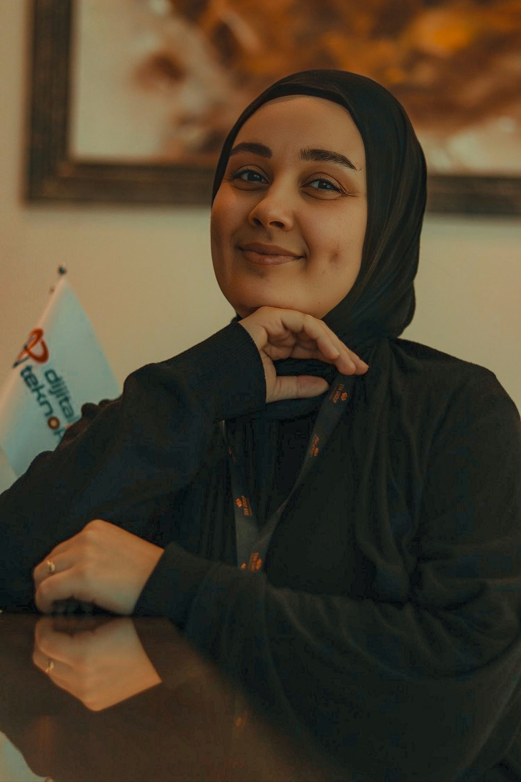 A cheerful woman in hijab poses thoughtfully, exuding warmth and positivity indoors.