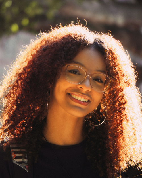 Free Portrait of a young woman with curly hair and eyeglasses smiling in natural light. Stock Photo