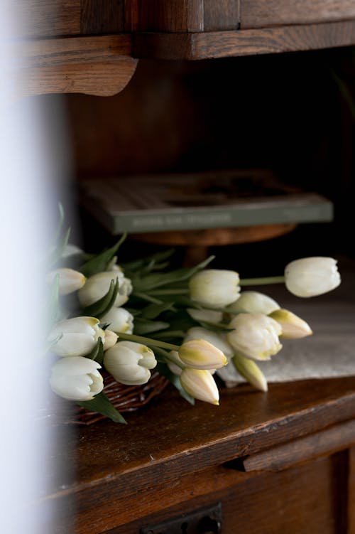 A vase of white tulips on a wooden table