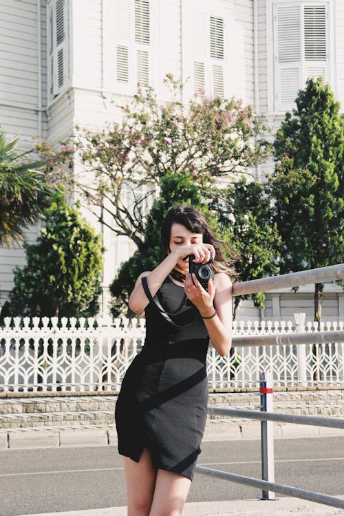 Gorgeous Brunette Woman in Black Dress Posing with Camera in Hands