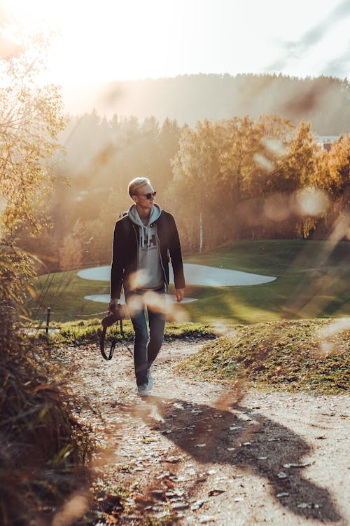 Free Man Walking and Holding Dslr Camera Near Tree Stock Photo