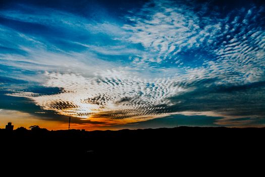 Dramatic sunset sky with vibrant colors and textured clouds casting silhouettes on hills.