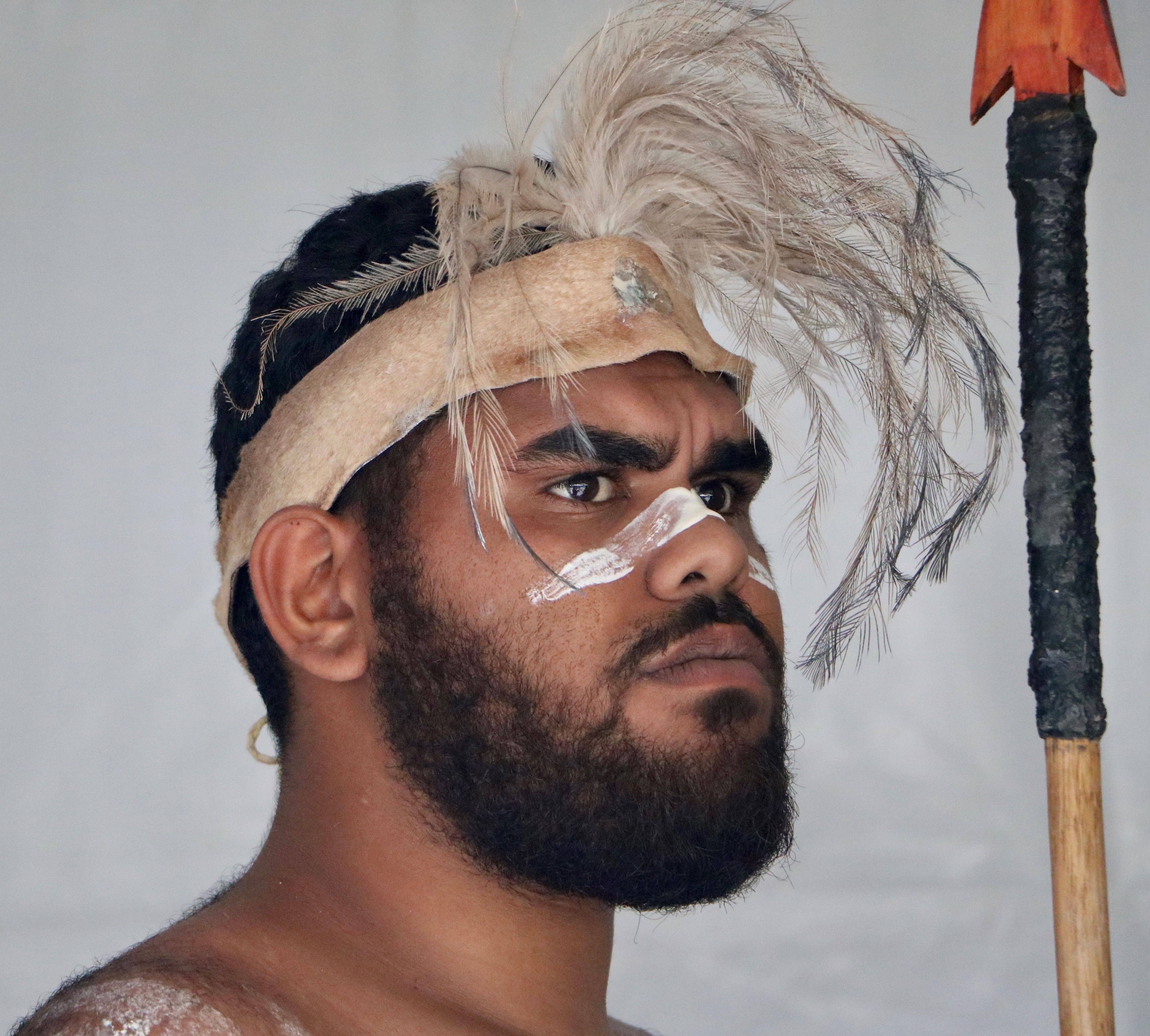 A fierce tribal warrior adorned with feathers and traditional makeup holds a spear, embodying cultural heritage.