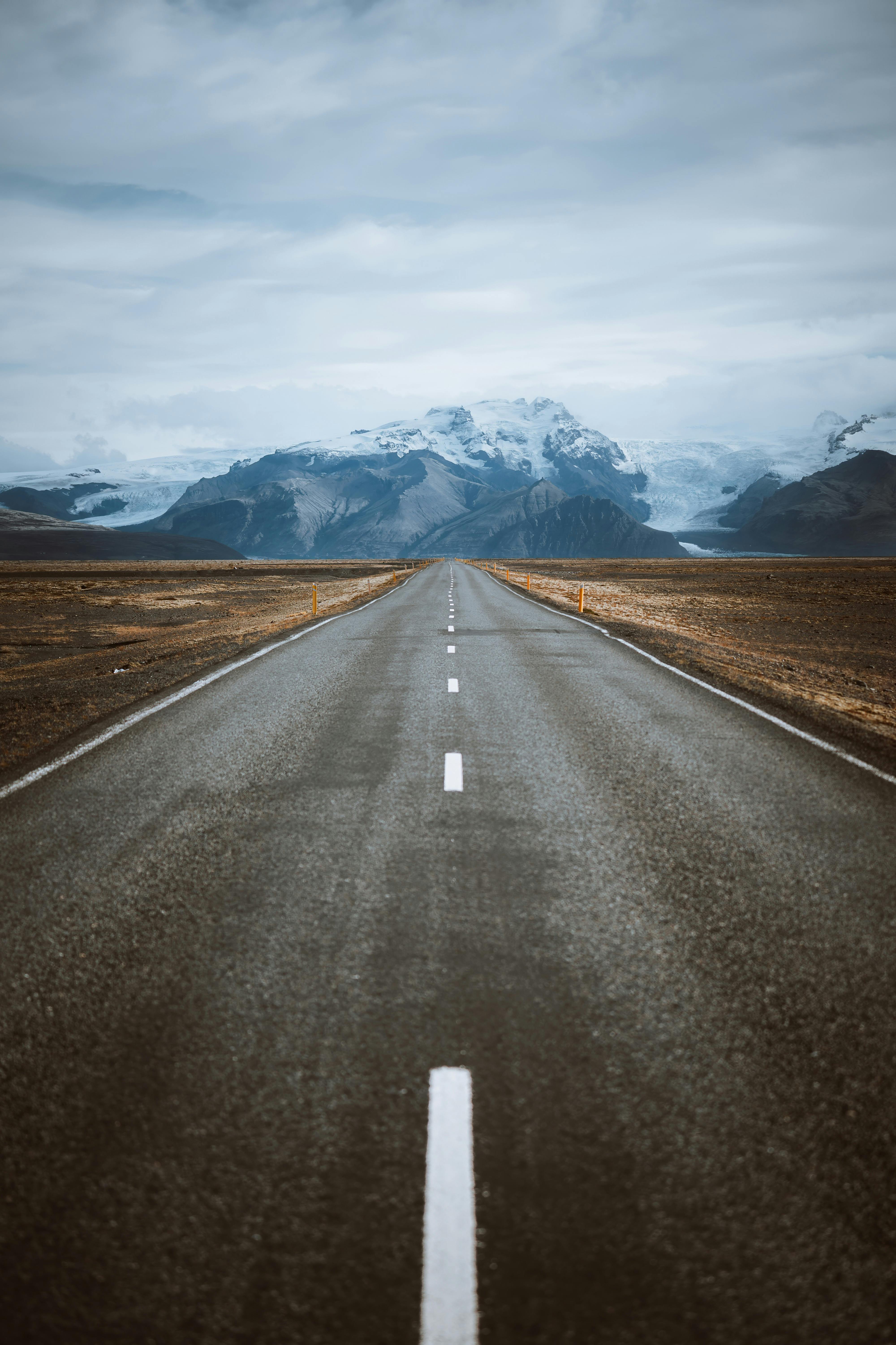 A mesmerizing road stretches towards snowcapped mountains, creating a breathtaking landscape view.