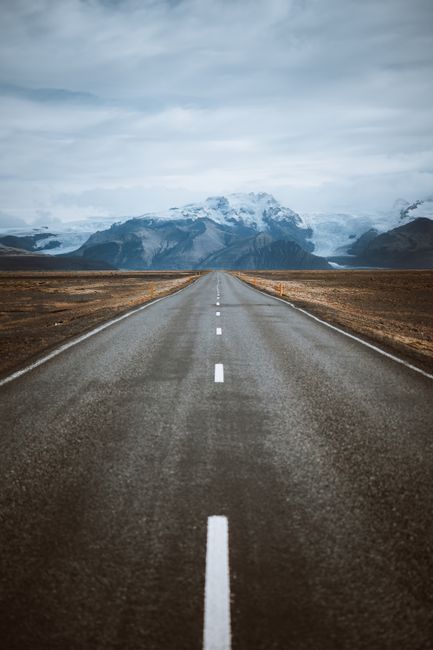 A mesmerizing road stretches towards snowcapped mountains, creating a breathtaking landscape view.