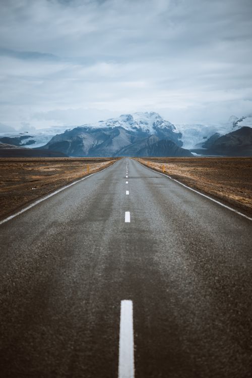 Free A mesmerizing road stretches towards snowcapped mountains, creating a breathtaking landscape view. Stock Photo