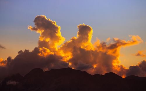 Free Dramatic clouds silhouetted against a mountain at sunset, creating a vivid and warm sky scene. Stock Photo