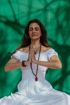 Calm and relaxed woman meditating outdoors with a vibrant green background.