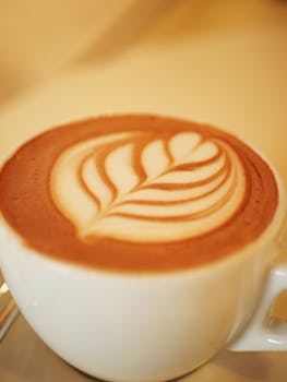 Close-up of a beautifully crafted latte with leaf foam art in a white cup, perfect for coffee lovers.