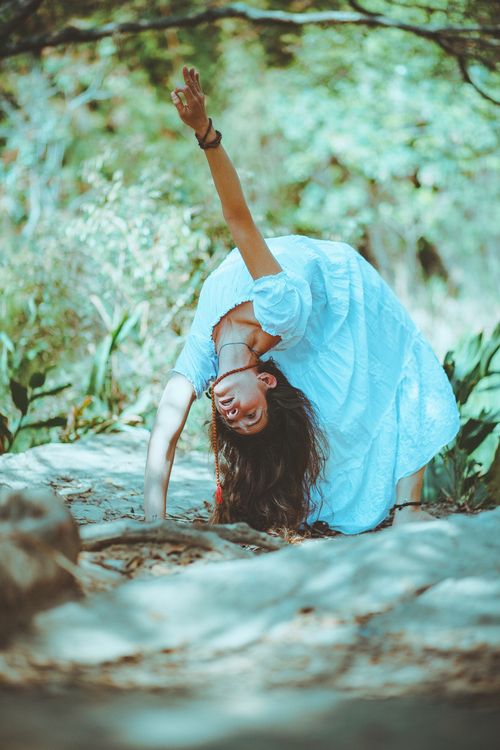Free A woman in a white dress bending gracefully in an outdoor setting, showcasing elegance and flexibility. Stock Photo