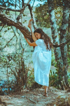 一位年轻女子身着白色连衣裙，在树林中赤脚优雅地摆着姿势